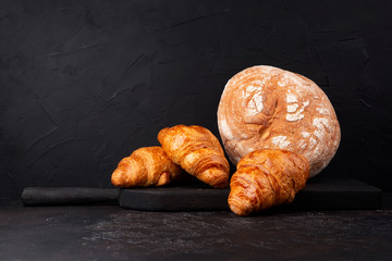 Fresh round bread and croissants on dark table. Copy space.