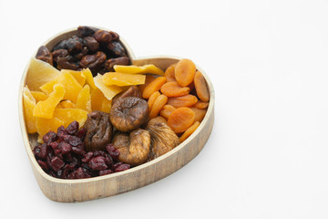 Fototapeta na wymiar Dried fruits mix, in wooden heart shape dbox isolated on white background. Top view of various dried fruits figs, apricots, mango, cranberries.