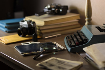 Fototapeta na wymiar Investigator desk with confidential documents, vintage typewriter, camera, magnifying glass. Secret documents investigation concept.