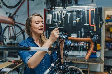Naklejka na ściany i meble Woman bicycle mechanic is repairing a bike in the workshop