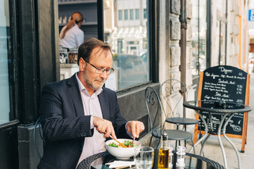 Businessman having lunch on a terrace in outdoor cafe, wearing a suit. Healthy green salad with salmon