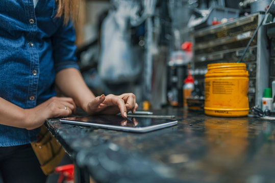 Female mechanic at work. Using a tablet while fixing a bicycle. Female bicycle repair technician using digital tablet in bicycle shop. Mechanic woman checking something on a tablet-pc and checklist.