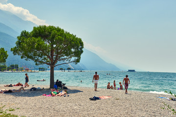 Riva del Garda,Lago di Garda ,Italy  - 21 June 2018: People who bathe and sit on the beach to tan at Lake Garda, beautiful Lake Garda surrounded by mountains in the summer time