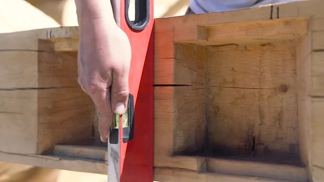 Close up of a carpenter hand installing construction level to the wooden beam. Clip. Process of wooden house building, professional equipment.