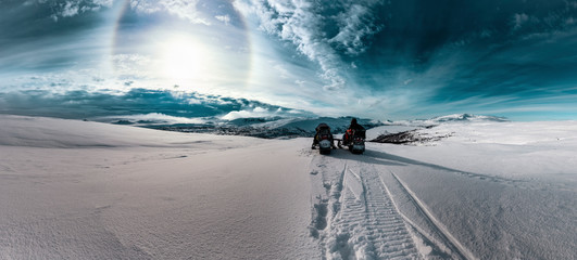 Two snowmobiles with one driver stand in front of dramatic scenic view at cold snowy Norwegian...