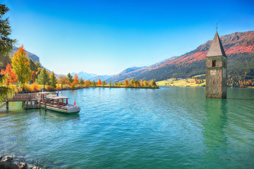 Fototapeta premium Fantastic autumn lake landscape with a ship near the pier and submerged bell tower in lake Resia