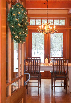 View through open front door of upscale winter vacation home interior beautiful, festive dining room with table set for Christmas dinner party, antler chandelier and  French doors windows.