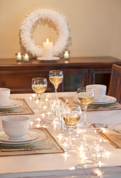 Beautiful, festive, home interior dining room table with candles, Christmas decorations, white china dishes and wine set for winter holiday dinner party