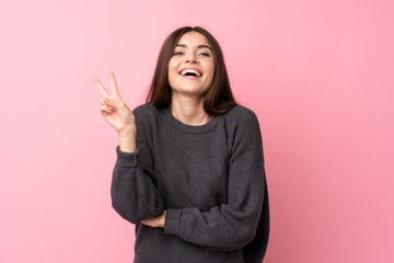 Young woman over isolated pink background smiling and showing victory sign