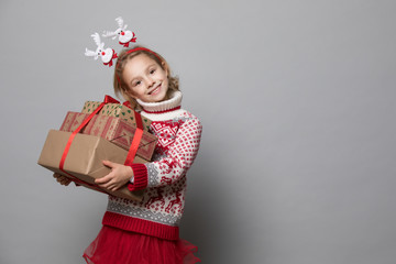 Smiling funny child in red sweater holding Christmas gift in hand.