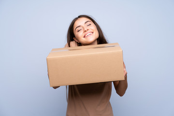 Young woman over isolated blue background holding a box to move it to another site