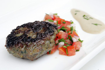 Kebab patty with tahini and chopped tomatoes.