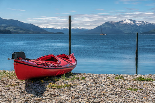 Red kayak is on the beach. Kayaking excursion in Alaska. Expedition on the sea.