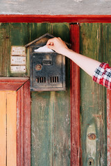 Woman's hand dropping a letter inside old-style metallic mailbox on the door