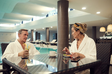 Portrait of wealthy senior couple relaxing in cafe at luxury SPA resort and eating dessert, copy...