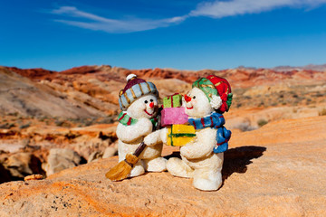Snowman Figurines in dry desert setting with mountains in the background.