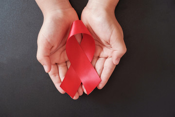 Hands holding red ribbon on black background, hiv awareness concept, world AIDS day, world hypertension day - obrazy, fototapety, plakaty