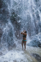 Fototapeta na wymiar Woman under waterfall, on the bottom of rocks and river.
