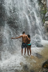 Fototapeta na wymiar Boyfriends under waterfall, on the bottom of rocks and river.