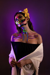 Retrato de joven maquillada de catrina con pintura neón iluminada con luz negra (uv light)