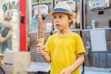 Little tourist boy eating 32 cm ice cream. 1 foot long ice cream. Long ice cream is a popular...