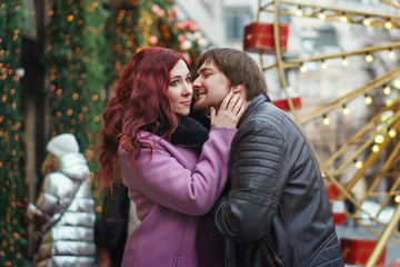 Loving couple in festive Christmas city celebrate the New Year. Romantic walk in winter. Having fun in winter christmas fair market decorations at central square city. Vacation and holiday concept