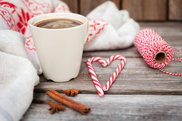 Cup of hot black coffee, knitted sweater with deer, candy cane and spices on wooden background. Winter background