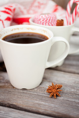 Cup of hot black coffee, knitted sweater with deer, candy cane and spices on wooden background. Winter background