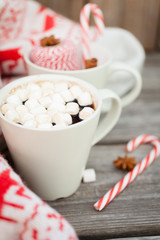 Coffee with marshmallows, knitted sweater with deer, candy cane on wooden background. Winter background