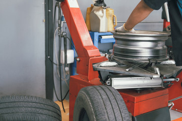 technician removing rubber from car wheel disc & balancing tyre on balancer in auto repair garage