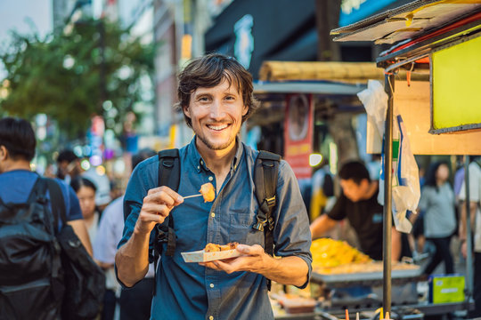 Young man tourist eating Typical Korean street food on a walking street of Seoul. Spicy fast food simply found at local Korean martket, Soul Korea