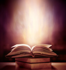 Open book on wooden vintage table with mystic magic bright light on background 