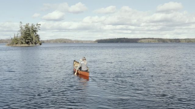 Aerial view of young female paddling in a canoe on a lake in the fall 04