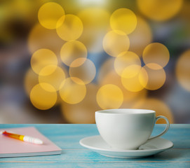 A cup of coffee and notrbook with abstract bokeh street light background