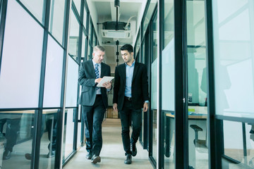 businessmen discussing work while walking in office corridor