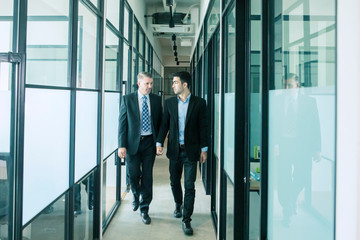 businessmen talking while walking in office corridor