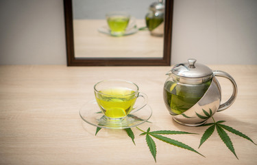 A glass of hot marijuana tea and tea pot on the table . Cannabis concept.