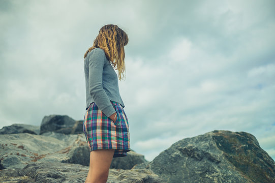 Young woman standing on some rocks against a cloudy sky