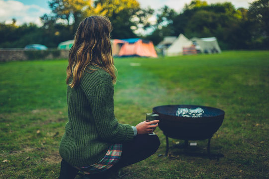 Young woman enjoying glass of wine by fire pit on campsite