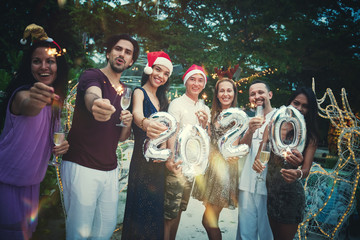 Group of happy people of mixed race friends celebrate Christmas and New Year at a tropical resort in Santa hats with shiny numbers in their hands.