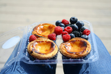 Traditional Portuguese dessert, pastel de nata and berries on knees