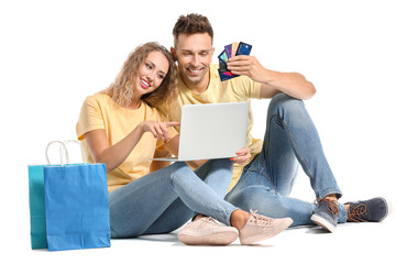 Young couple with credit cards, shopping bags and laptop on white background