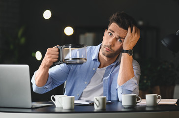 Tired man drinking coffee and trying to meet deadline in office