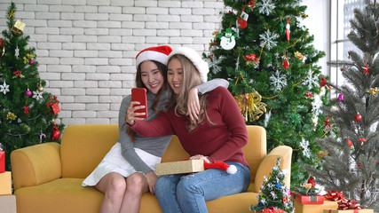 Asian women smiling and showing gift, taking a selfie by mobile smartphone in Christmas holiday