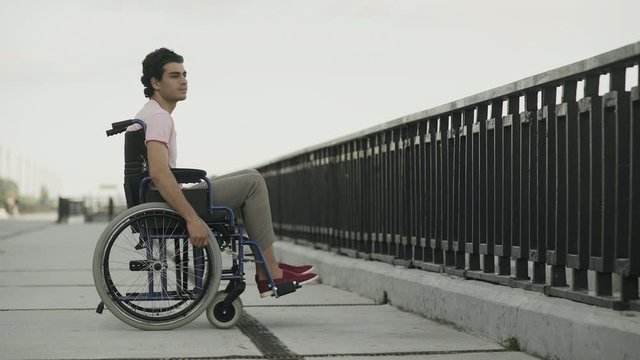 Thoughtful young man sitting on wheelchair. Sad disabled on wheelchair outside feeling lonely.