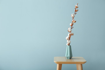 Naklejka premium Vase with beautiful cotton flowers on table against color background
