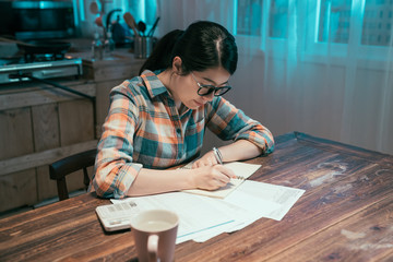 Fototapeta na wymiar attractive young asian korean housewife wears glasses at home stay up late in night. girl examines gas and electricity bills. female considers spending this month and under stress checking accounts