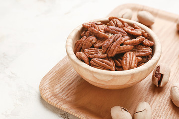 Bowl with tasty pecan nuts on light background