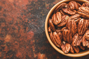 Bowl with tasty pecan nuts on color background