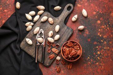 Bowl with tasty pecan nuts, nutcracker and board on color background
